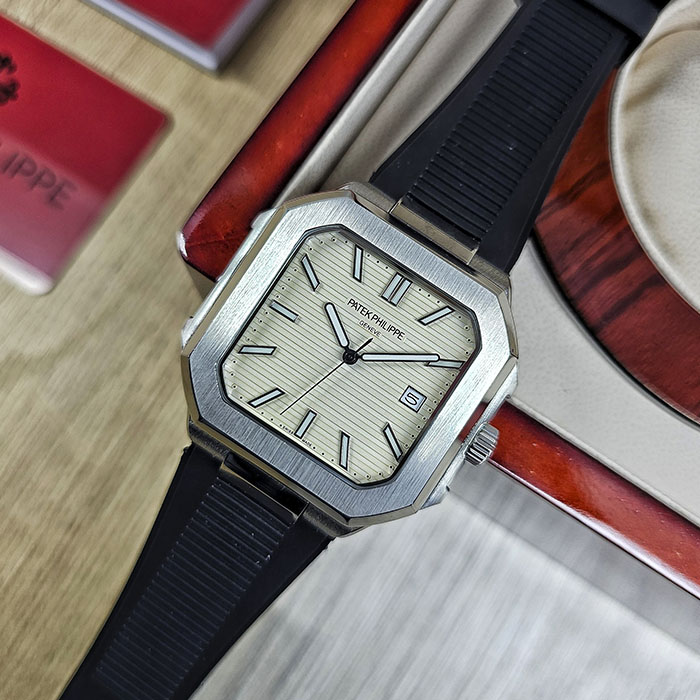 Réplica de reloj Patek Philippe Cubitus calidad AAA en caja de acero con esfera beige crema acanalada, fecha a las 3 y correa de caucho negra.