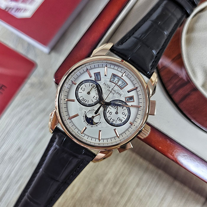 Réplica AAA de reloj Patek Philippe en caja de oro rosa con dial plata grabado en guilloché, indicador panorámico de fecha y correa negra.
