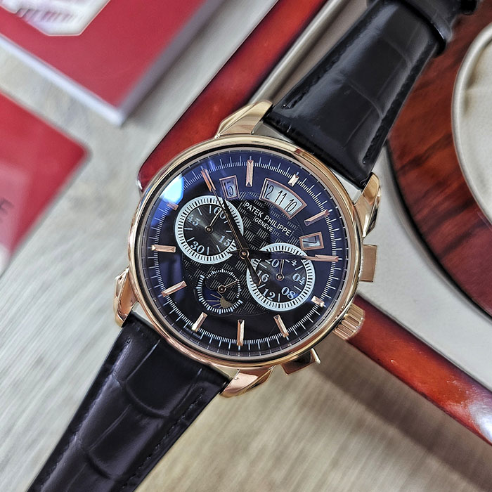 Réplica de reloj Patek Philippe calidad AAA en caja de oro rosa con dial negro grabado, subesferas de cronógrafo, fecha y correa de cuero negra.