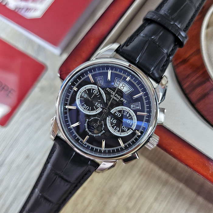 Réplica AAA de reloj Patek Philippe en caja de acero inoxidable con esfera negra grabada, subesferas funcionales y correa de cuero negra.