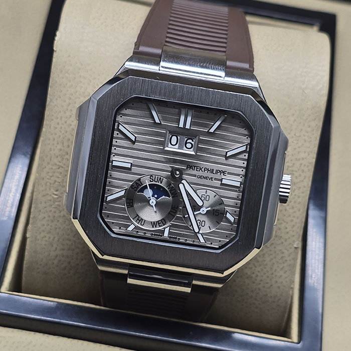 Réplica AAA de reloj Patek Philippe Cubitus con caja de acero, esfera gris ahumada, gran fecha panorámica y correa de caucho marrón.