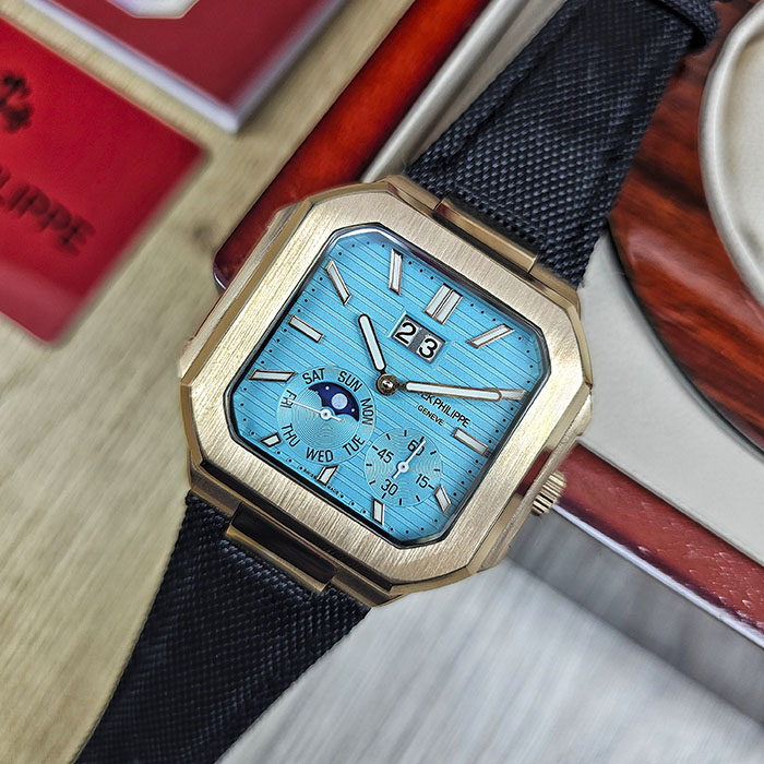 Réplica AAA Patek Philippe Cubitus en caja de oro rosa con brillante esfera azul turquesa, gran fecha panorámica y correa de tela negra.