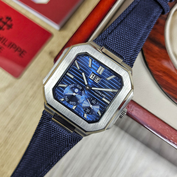 Réplica AAA de reloj Patek Philippe Cubitus en caja de acero con esfera azul acanalada, gran fechador, fase lunar y correa textil azul marino.
