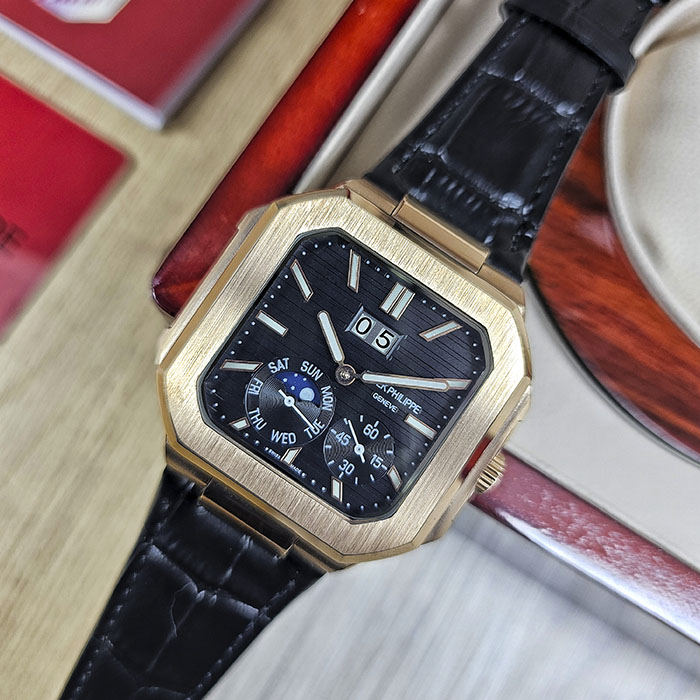 Réplica AAA de reloj Patek Philippe Cubitus en caja de oro rosa con imponente esfera negra acanalada, gran fecha panorámica y correa de cuero negra.