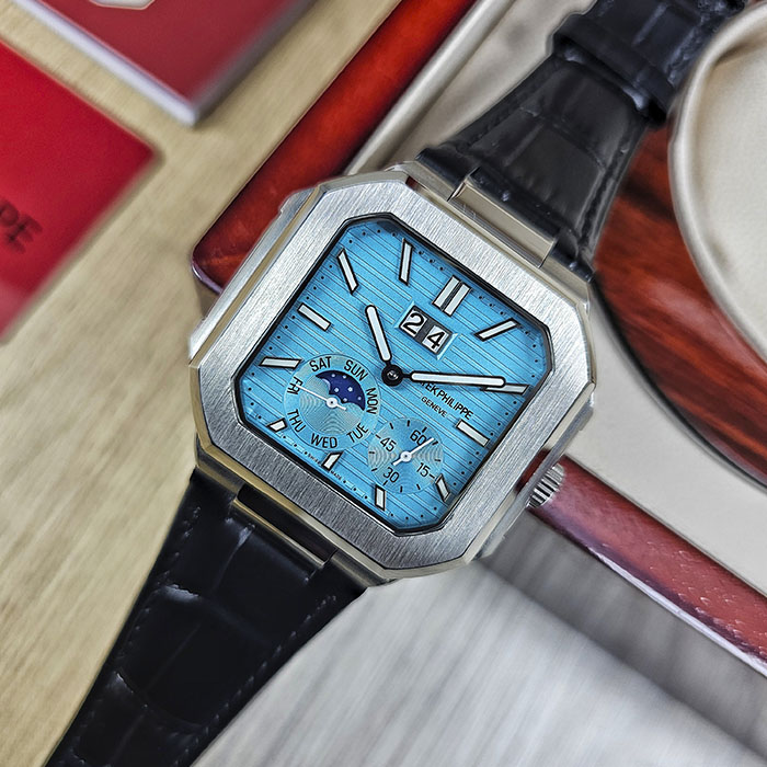 Réplica AAA Patek Philippe Cubitus en caja de acero con esfera azul turquesa acanalada, gran fecha, fase lunar y correa de cuero negra.